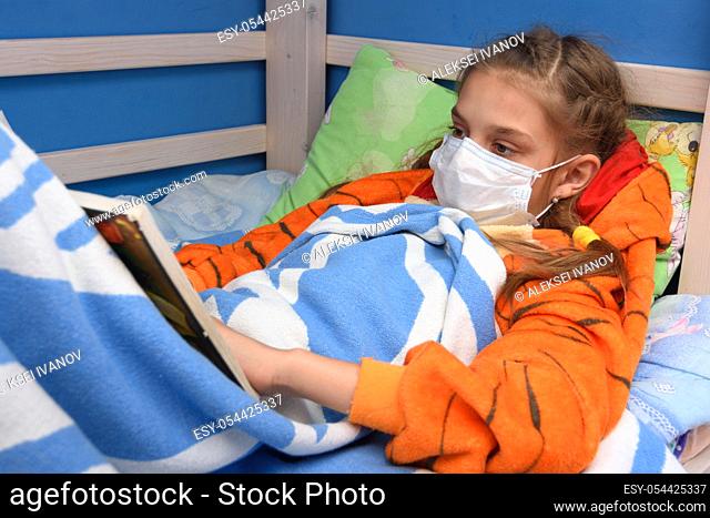 Sick girl in medical mask lies in bed and reads a book