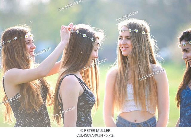 Teenage girls putting on and wearing daisy chain headdresses in park