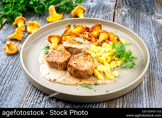 Modern style traditional barbecue pork filet medaillons in cream sauce with chanterelle mushrooms and spaetzle offered as close-up on a Nordic design plate