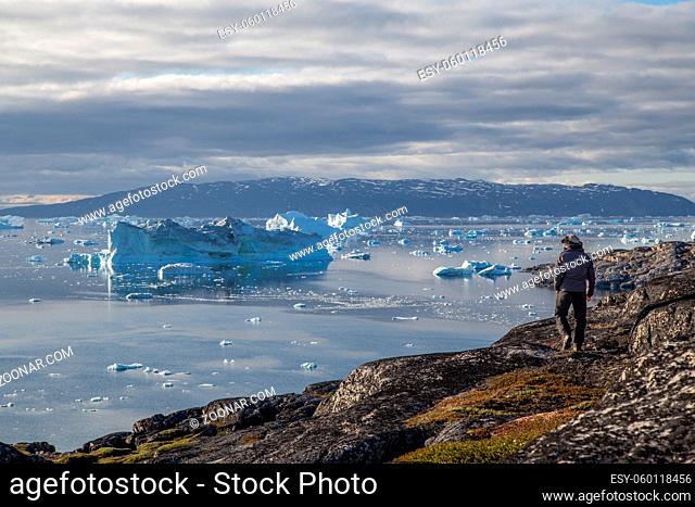 Rodebay, Greenland - July 09, 2018: A man is walking and looking at icebergs. Rodebay, also known as Oqaatsut is a fishing settlement north of Ilulissat