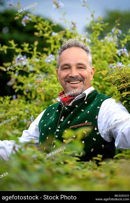 Laughing middle-aged man in Bavarian traditional costume standing by a hedge, Karlsruhe, Germany, Europe