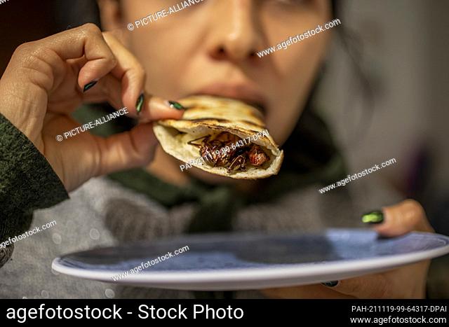 18 November 2021, Mexico, Mexiko-Stadt: A woman tastes a quesadilla with migratory locusts at a market. Insects are very common in Mexican cuisine