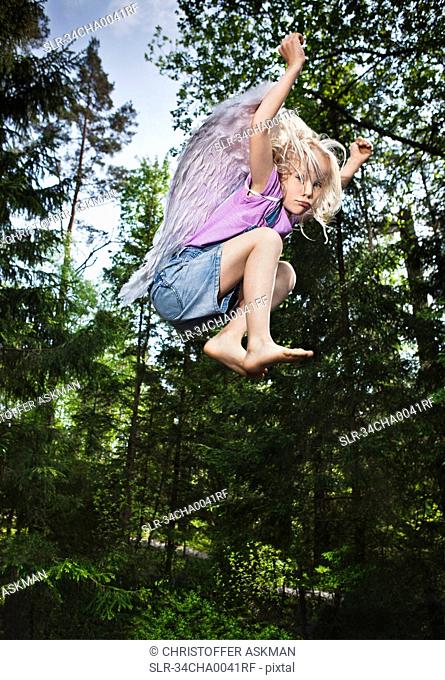 Girl wearing wings and jumping in forest