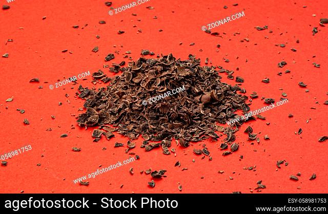 Milled chocolate. Pile of ground chocolate on red background, closeup