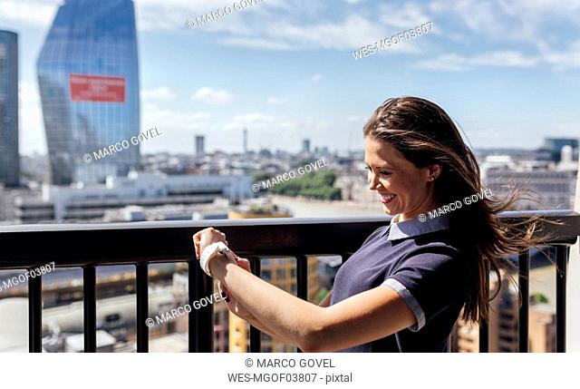 UK, London, happy woman using smartwatch on a roof terrace