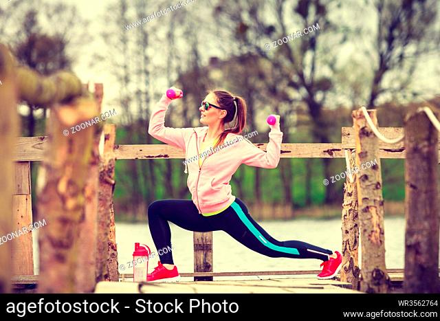 Woman doing sports outdoors with dumbbells lifting weights. Fit fitness girl in sportswear exercising outside on fresh air