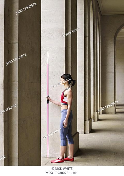 Female athlete holding javelin standing in portico side view