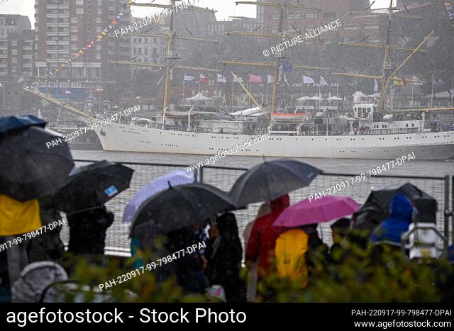 17 September 2022, Hamburg: Onlookers stand with umbrellas in the rain in front of the Polish sail training ship Dar Mlodziezy moored at the landing stages