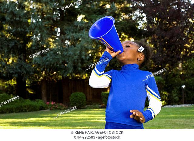 A little black girl dressed as a cheerleader for Halloween yelling through a megaphone
