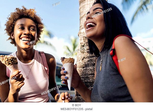 Two happy female friends with ice cream cones at a palm tree
