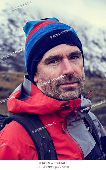 Male hiker in knit hat by snow capped mountains, close up portrait, Llanberis, Gwynedd, Wales