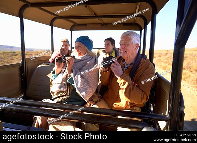 Happy seniors with binoculars and camera on safari in off-road vehicle