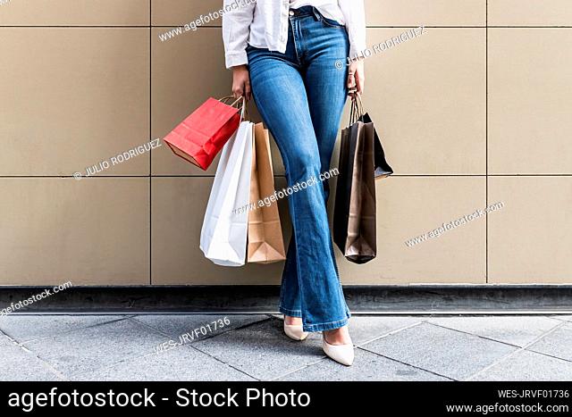 Young woman holding shopping bags while standing on footpath
