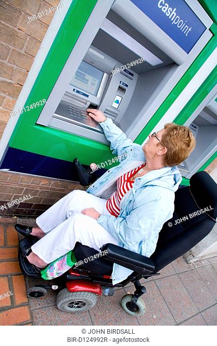 Older woman wheelchair user using a cashpoint machine