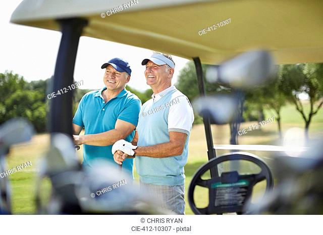 Senior men standing next to golf cart