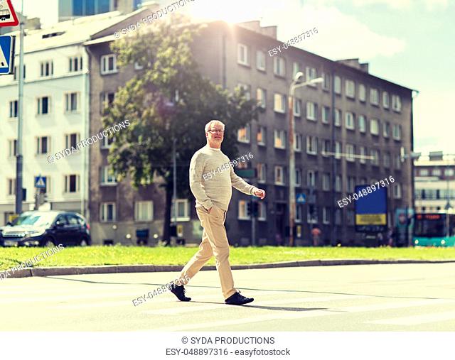 senior man walking along city crosswalk