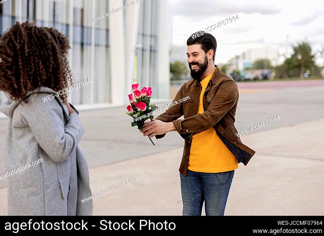 Happy young man giving bouquet of flowers to woman at footpath
