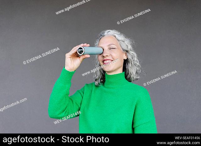 Smiling woman looking through monocular in front of wall