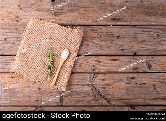 Directly above shot of rock salt in wooden spoon and rosemary on jute fabric at table