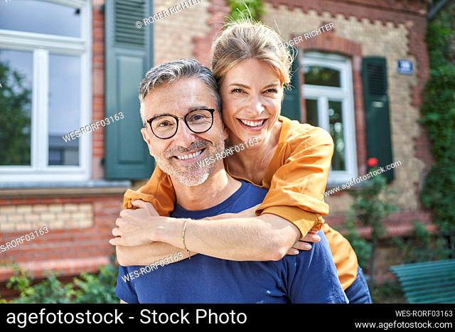 Happy woman embracing mature man from behind in front of house