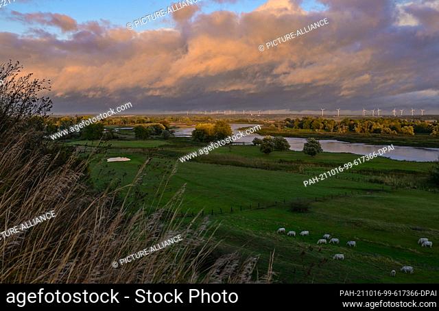 15 October 2021, Brandenburg, Lebus: Dark rain clouds are bathed in a warm light over the German-Polish border river Oder by the light of the evening sun