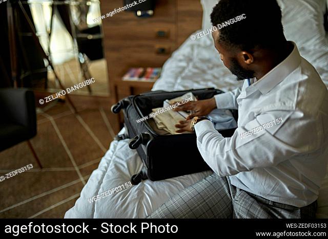 Businessman sitting on bed in hotel room packing his suitcase
