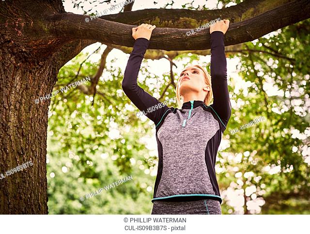 Young woman doing pull ups on park tree branch