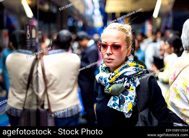 Young woman wearing colorful scarf waiting on the platform of a urban metro station for train to arrive. Public transport