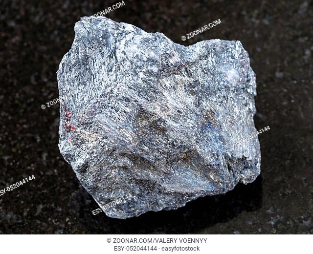 macro shooting of natural mineral rock specimen - rough antimony ore (Stibnite) stone on dark granite background from Ukraine