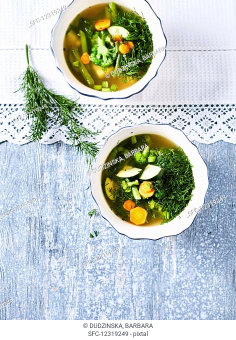 Vegan green minestrone soup with zucchini, cabbage, broccoli, beans and dill (top view)
