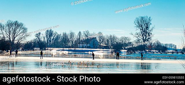 Wagenignen, The Netherlands - February 13, 2021: Ice skaters having fun in the sun on frozen floodplains along river Rhine in Holland
