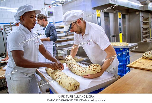 18 October 2019, Saxony, Dresden: Moussa Duale (l) from Guinea and baker Sylvio Beck (r) prepare large Christmas stollen for baking in the Dresden bakery
