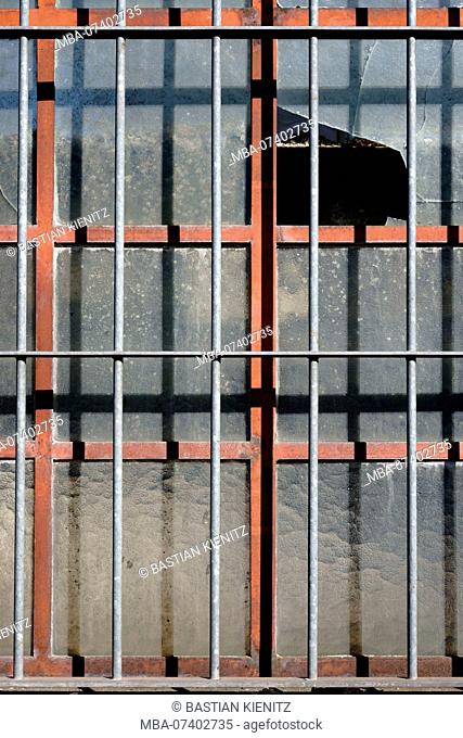 A broken window of a disused industrial building with a barred window