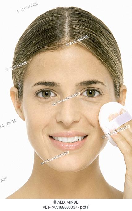 Woman using powder puff on cheek, smiling at camera, close-up