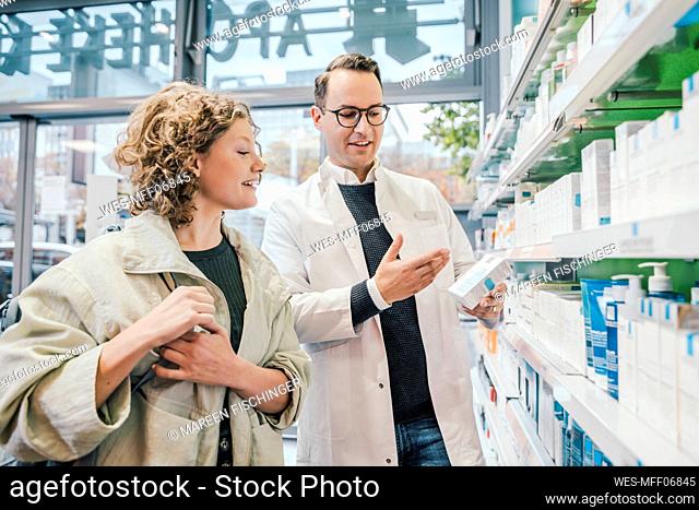 Pharmacist recommending medicine to smiling customer in chemist shop