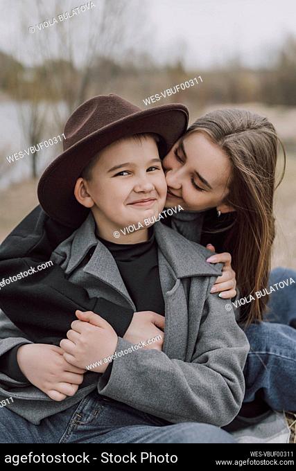 Mother embracing happy son sitting on field