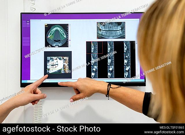 Female dentist and patient pointing at digital image on screen at medical clinic