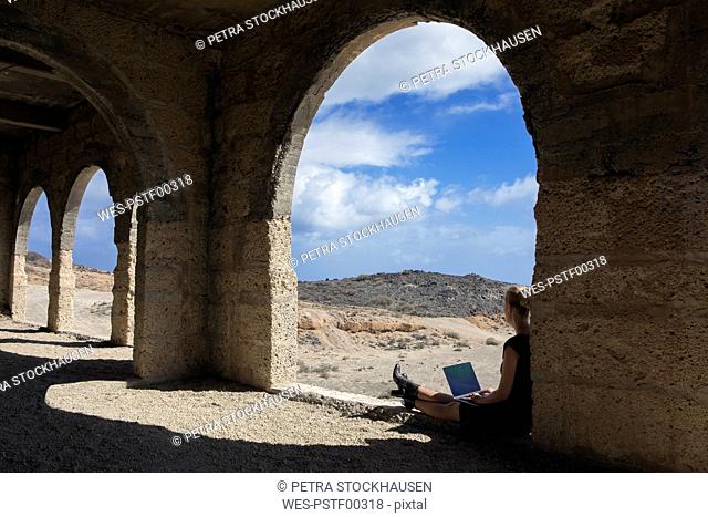 Spain, Tenerife, Abades, Sanatorio de Abona, woman sitting in ghost town building using laptop