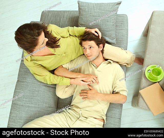 Young couple resting together on couch at home, embracing. Hing angle shot