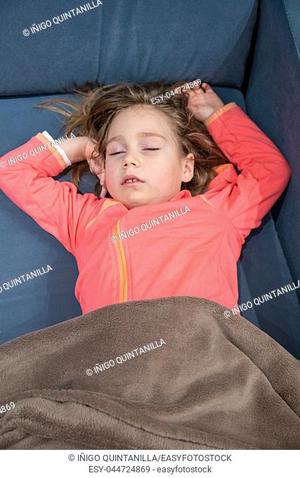 above view of face of blonde caucasian five years old child, lying on her back on blue sofa, sleeping pleasantly