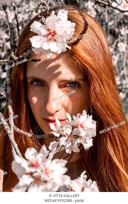 Portrait of redheaded woman behind twigs of blossoming tree