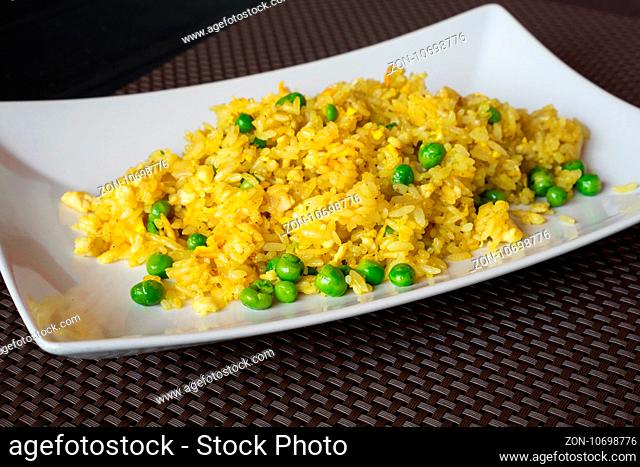 Fried curry rice with peas served on white plate at restaurant, brown background