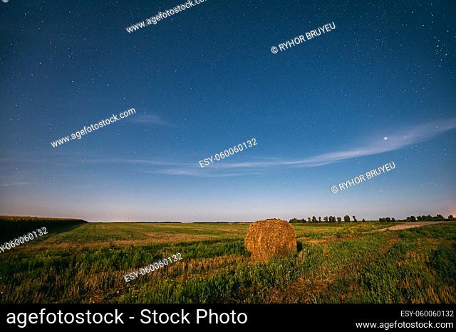 Natural Night Starry Sky Above Field Meadow With Hay Bale After Harvest. Glowing Stars Above Rural Landscape In August Month. Agricultural Landscape