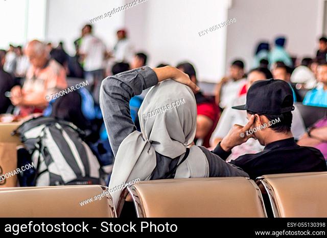 Modern muslim islamic asian couple sitting and waiting for flight departure at international airport terminal