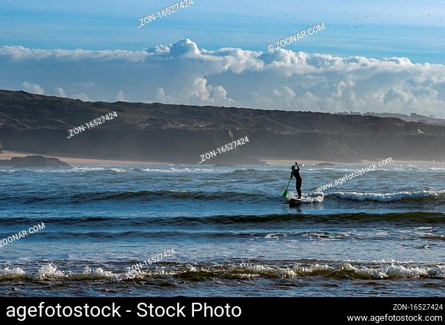 Vila Nova de Milfontes, Portugal: 23 December 2020: surfer enjoys catching waves on a SUP paddleboard at Milfontes beach