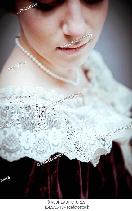 Young woman with short brown hair wearing period dress with lace collar and pearl necklace