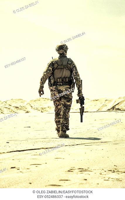 Military contractor, army infantry or rifleman in camouflage uniform and helmet patrolling territory in desert. Airsoft player with real firearm replica walking...