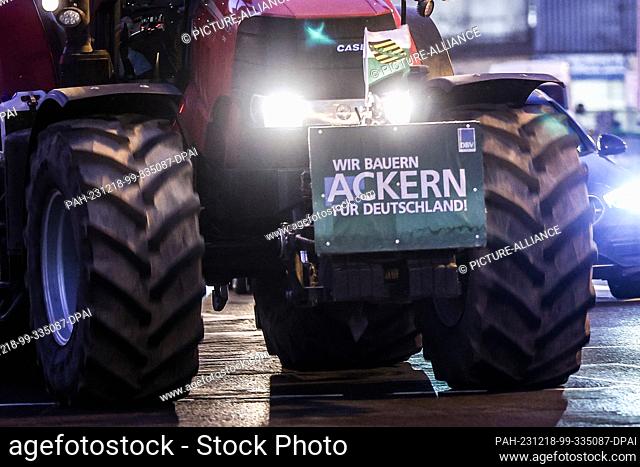 18 December 2023, Saxony, Leipzig: One of several farmers drives through the early morning rush hour traffic with his tractor and a protest poster