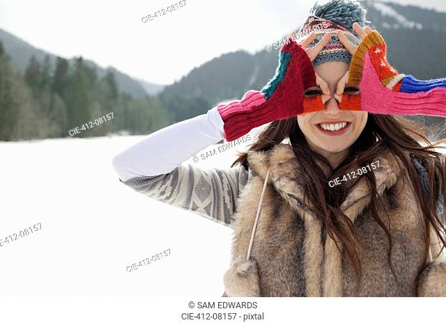 Portrait of smiling woman circling eyes with fingers in snowy field