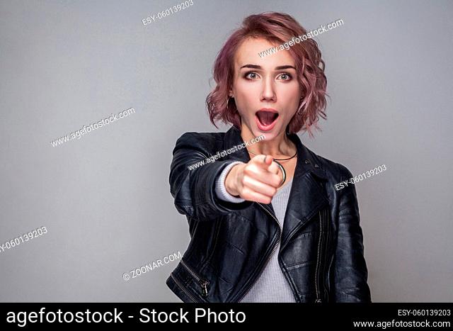 Portrait of surprised beautiful girl with short hairstyle and makeup in black leather jacket standing, pointing and looking at camera with amazed face